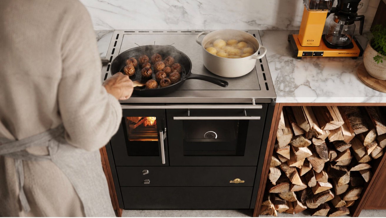 Person som steker köttbullar och kokar potatis på en vedeldad köksspis